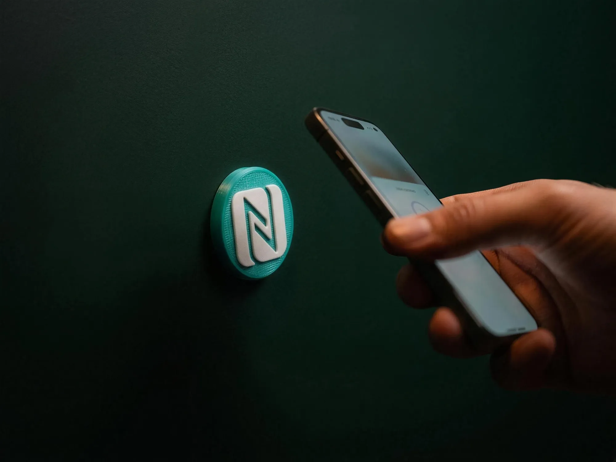Turquoise Tapora NFC badge on a wall being tapped with a phone